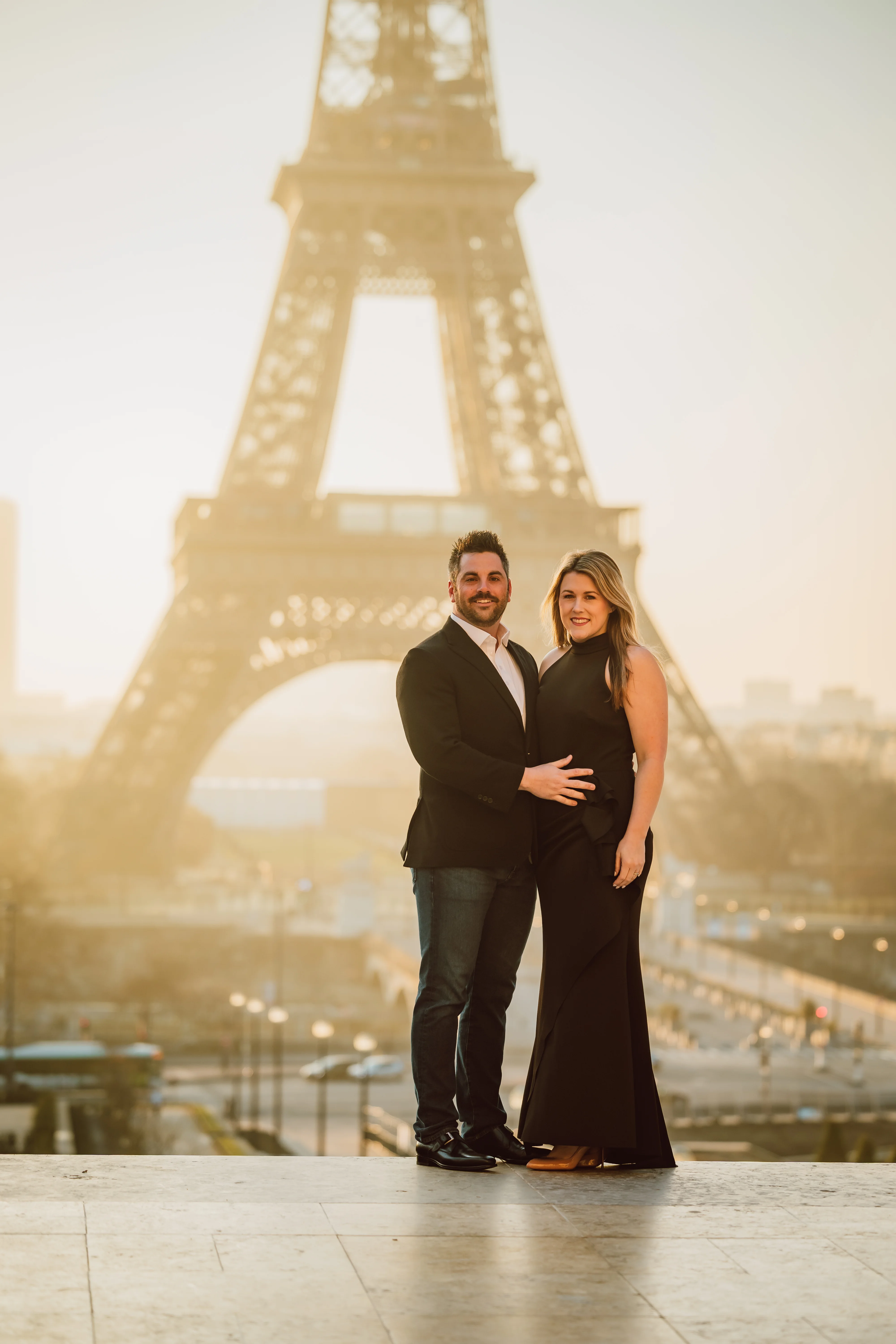Couple in formal black attire posing together with architectural landmark in background